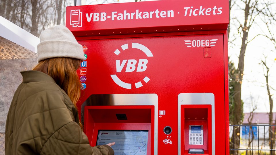 Ein Fahrgast, der vor einem roten VBB-Fahrkartenautomaten steht