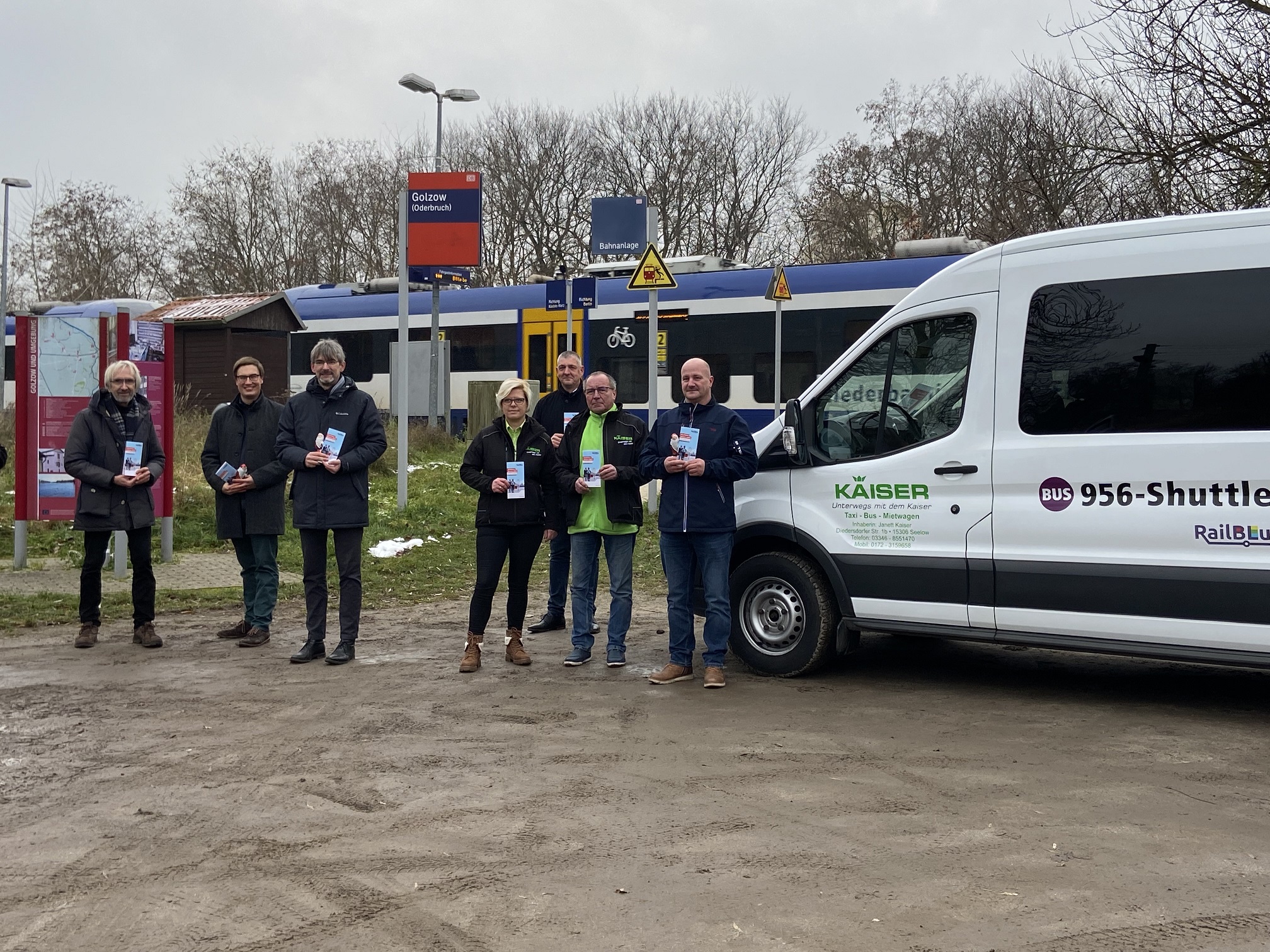Shuttlebus Golzow Shuttlebus direkt vor dem Bahnsteig mit dem Zug der Linie RB26 im Hintergrund. Links neben dem Bus stehen Jürgen-Peter Hiller vom Ministerium für Infrastruktur und Landesplanung, Max Goethel vom VBB, Golzows Bürgermeister Frank Schütz, Busunternehmerin Janett Kaiser, Torsten Heisler von der mobus Märkisch-Oderland Bus GmbH, Dietmar Kaiser vom Busunternehmen Kaiser und Heiko Arndt von der mobus Märkisch-Oderland Bus GmbH.